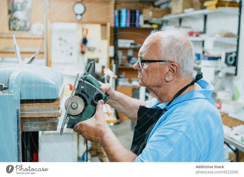 Focused elderly male master using circular saw in workshop man woodwork carpenter concentrate tool professional occupation senior apron eyeglasses artisan job