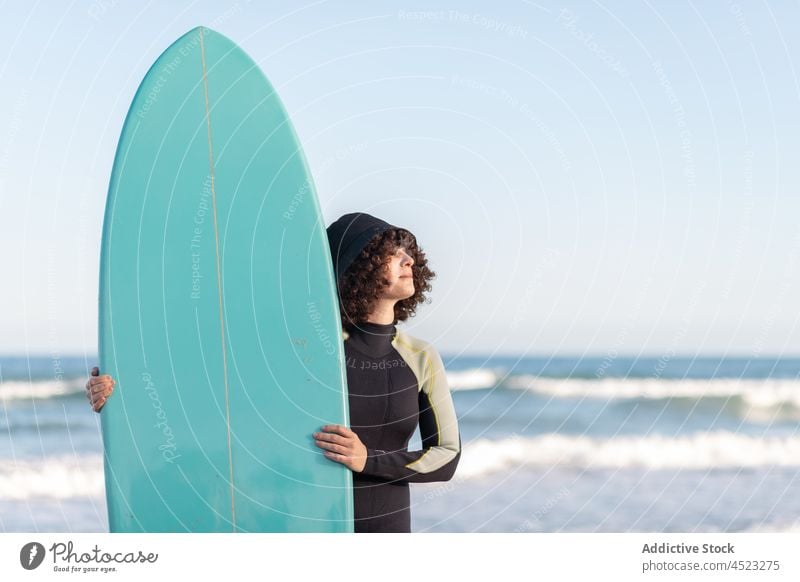 Curly haired woman with surfboard on sea shore surfer tropical beach wave foam carefree activity female seashore wetsuit coast water cloudless sky bay scenery