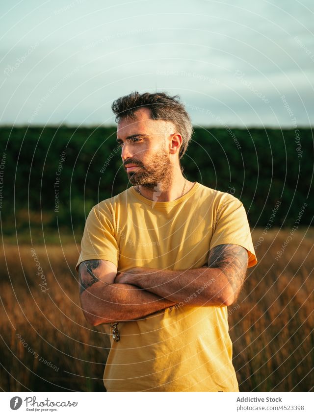 Serious bearded man standing in field nature countryside meadow brutal tattoo masculine leisure pastime grassy male confident summer environment serious t shirt