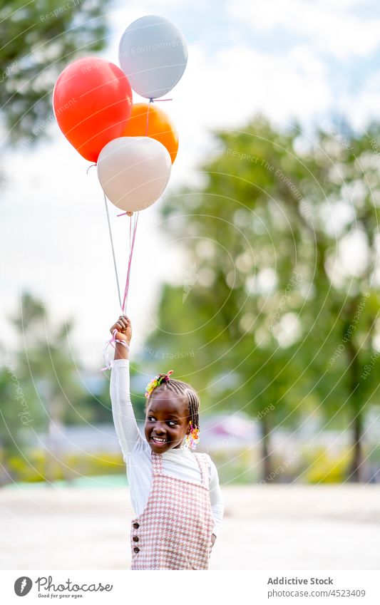Happy black girl running with colorful balloons cheerful kid smile style positive park happy child african american ethnic outfit fun bright joy braid daytime