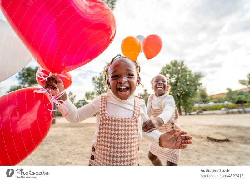 Positive black girls with balloons standing on grass in park children smile happy sister dress positive joy kid african american little similar ethnic friend