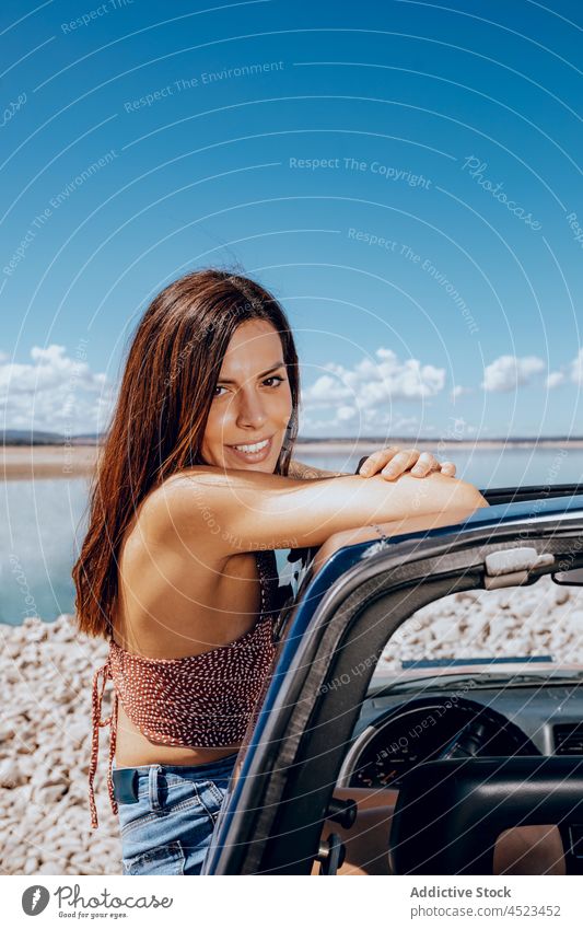 Young woman leaning out from car relax pond carefree window freedom shore chill nature female coast transport river traveler denim blue sky landscape sunbeam