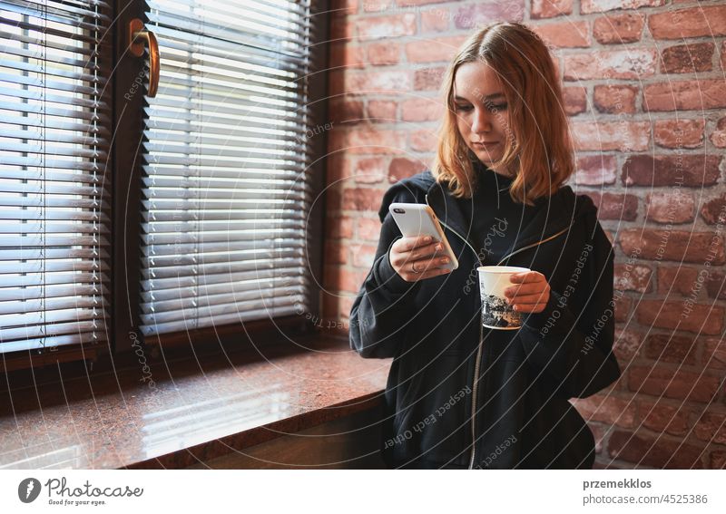 Woman texting on smartphone, drinking coffee while taking a break in office using mobile person indoor working holding cellphone mobile phone smart phone
