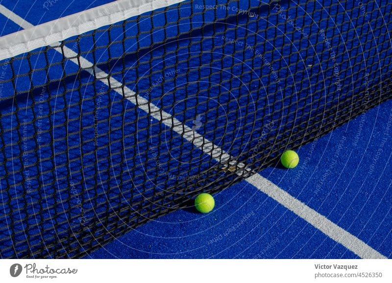 Twoo balls next to the net of a blue paddle tennis court. shadows padel court courts padel tennis texture ground still life lawn artificial grass athletics