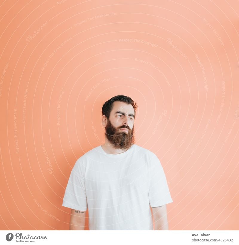 Young hipster bearded man looking away from camera, copy space, soft orange removable background, minimal basic, ad concept deal, white shirt space male