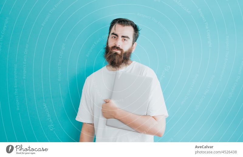 Young hipster bearded man holding a laptop, copy space, soft blue removable background, minimal basic, student, entrepreneur concept, white shirt space guy male