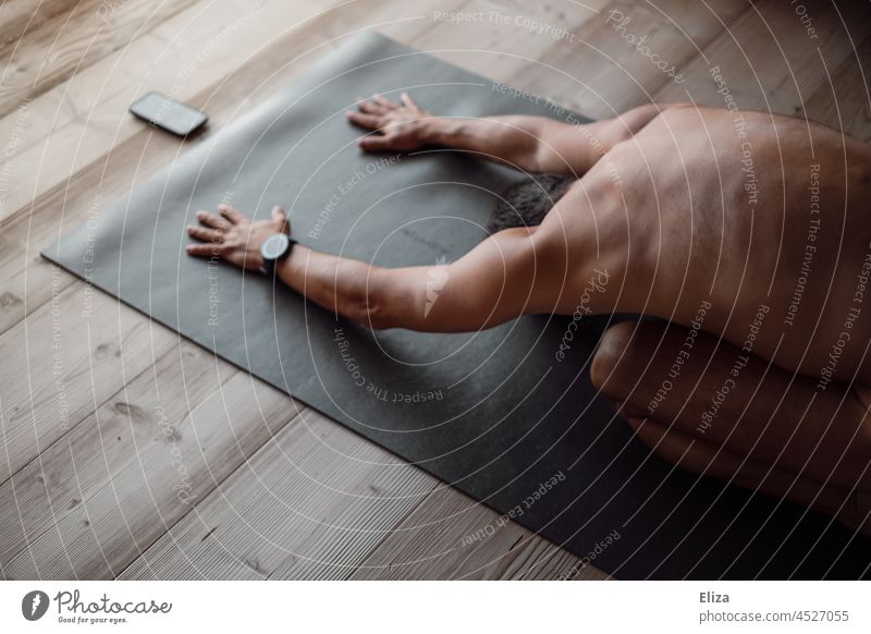 A man does yoga exercises on a yoga mat at home with a course on his phone Yoga Man Naked Lifestyle Cellphone Telephone Fitness wooden floor Black Yoga posture