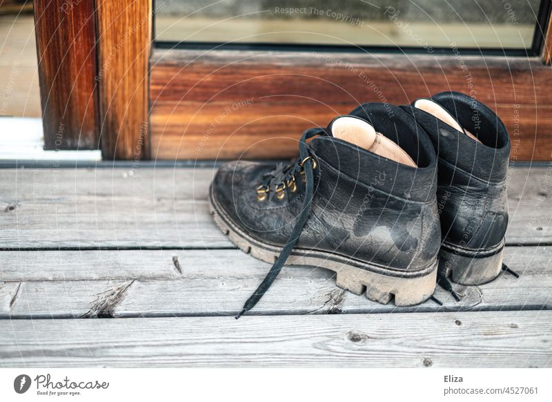 Dusty hiking boots in front of the patio door Hiking boots Patio door Footwear Black Leather Boots Wood Pair of shoes Dirty outdoor Leather shoes
