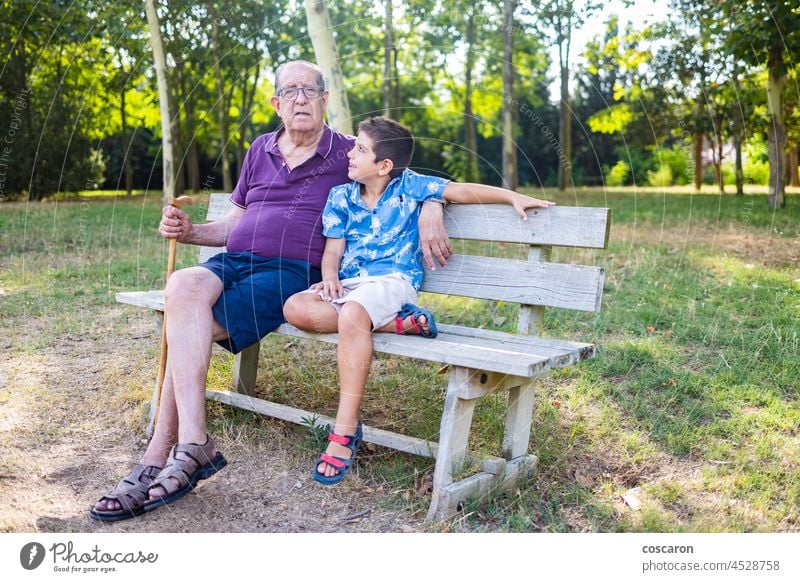 Grandfather and his grandson sitting on a bench in the park activity aging boy child childhood elderly family friends generation grandchild grandfather