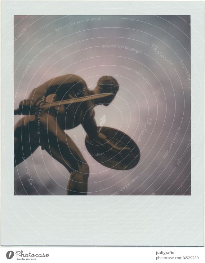 Gold plated sculpture of a warrior on polaroid Sculpture Warrior Fighter Man Weapon Force Soldier Battle sign Sword Combat Light Eerie Sky Dynamics Polaroid