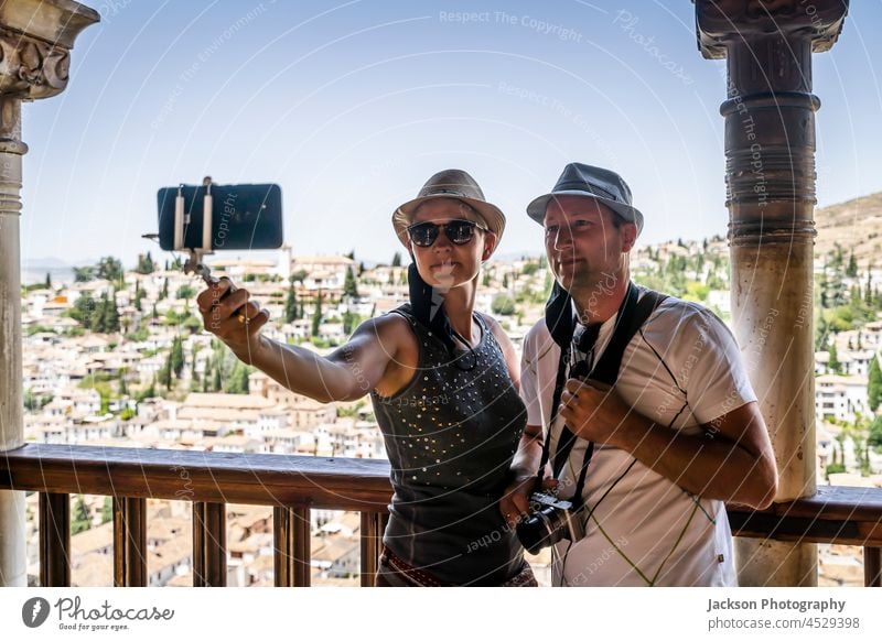 A tourist couple taking selfie in the Alhambra palace with the view of Granada, Spain take smartphone spain adult alhambra architecture camera caucasian