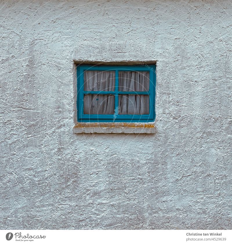 A small blue mullioned window with drawn curtains in a roughly plastered white wall Window Lattice window blue window Window board Window frame Rendered facade