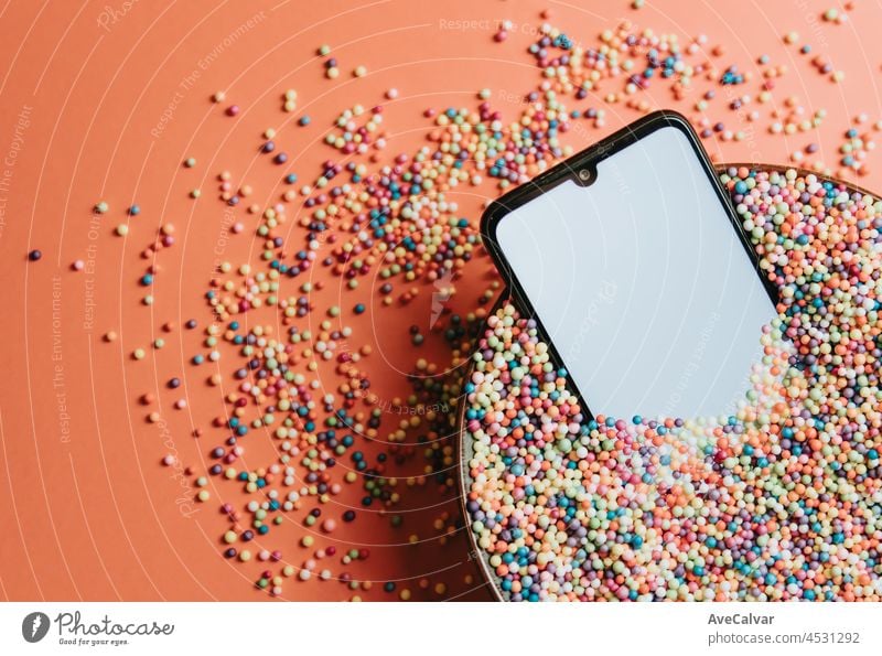 Fancy colorful image of a mobile phone in a bowl of colorful balls with blank screen with copy space, kid image, party social network style cyberspace gadget
