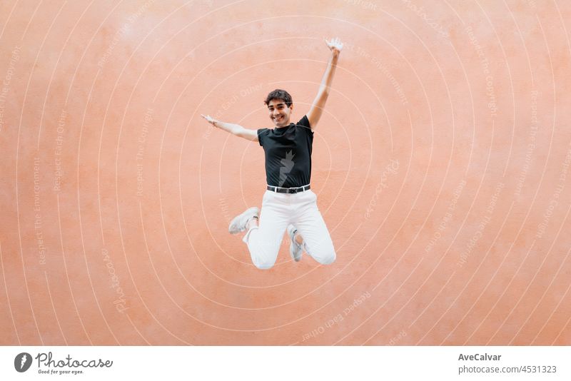 Young man on urban clothing falling and jumping in front of a massive orange wall, copy space, ad image, liberty and freedom concepts, city life, life in the city, adventure concept, lgbt
