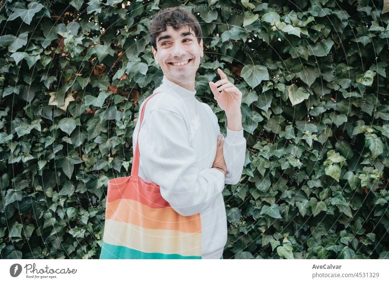 Portrait of a young lgbt man with a tote bag of rainbow pride flag smiling away from camera, city gay pride life style, best time of the day, social network