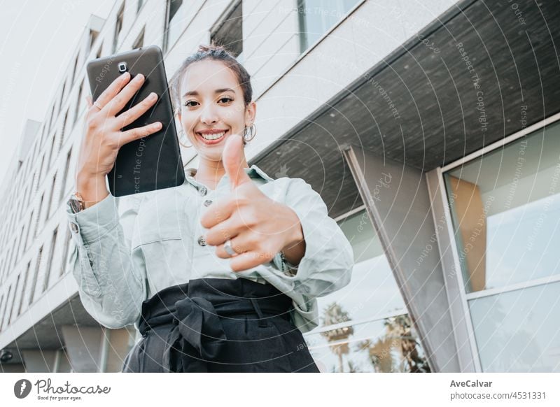 Young entrepreneur mixed race woman holding a tablet saying ok to camera, office and business concept, copy space, outdoors, well dressed businesswoman young