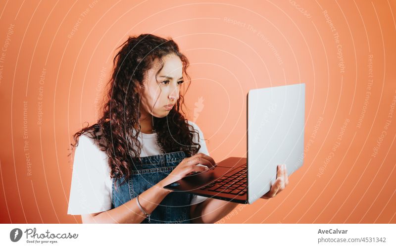 Young mixed race woman holding a laptop and worried about something she is seeing on the screen, orange background removable background, minimal image, copy space, basic situations