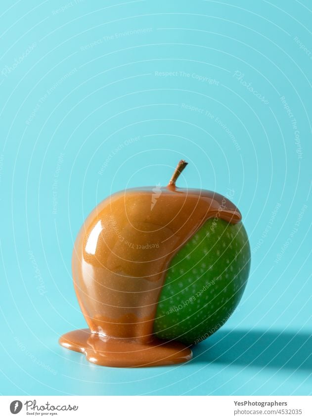 Caramel apple isolated on a blue background. Green apple covered in caramel sauce brown calories candy christmas close-up color condensed cream cuisine cut out