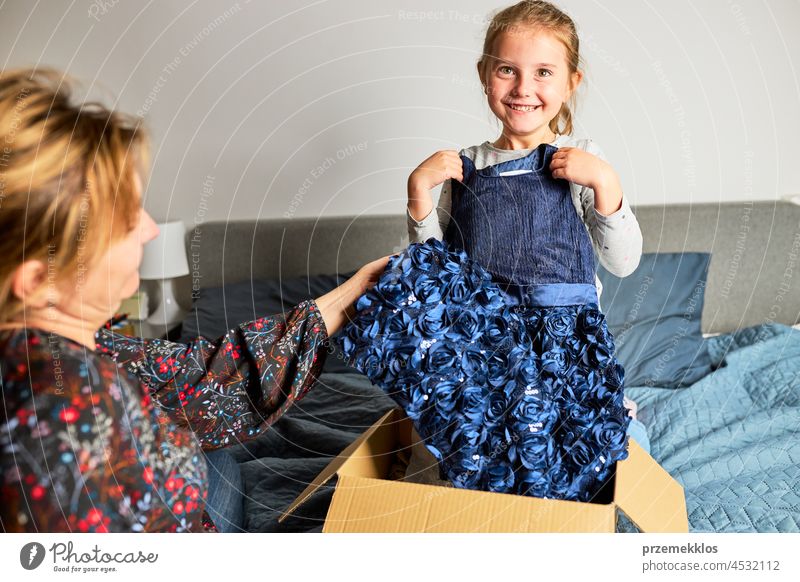 Mother and her daughter opening box with ordered dress. Online shopper customer holding dress online shopping unpacking gift present girl package home buy