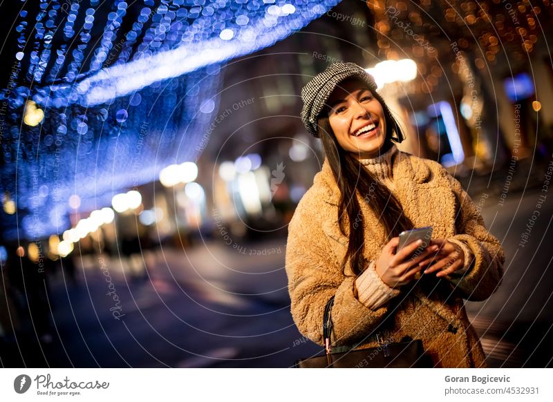 Pretty young woman using her mobile phone in the street at Christmas time bag beautiful browsing cap cellphone christmas city cityscape communication concept