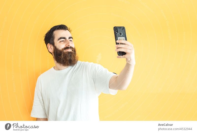 Young hipster bearded man taking a selfie on his phone, blank space, copy space, soft yellow removable background, minimal basic, ad concept deal, white shirt space