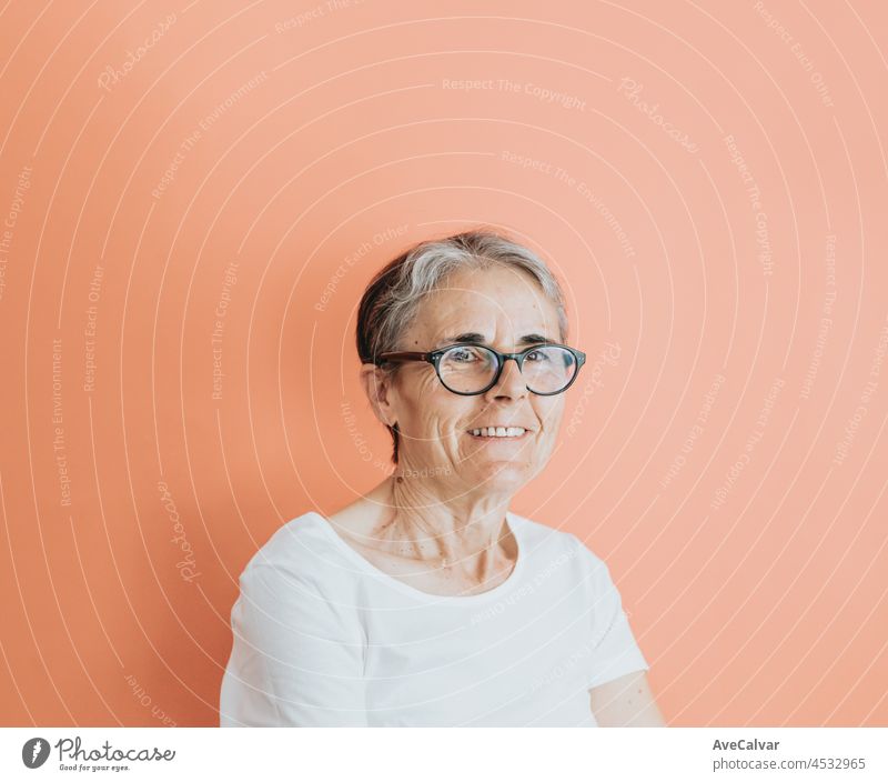 Old woman doing smiling to camera, copy space, soft orange removable background, minimal basic, old people lifestyle, ad concept deal, white shirt space senior