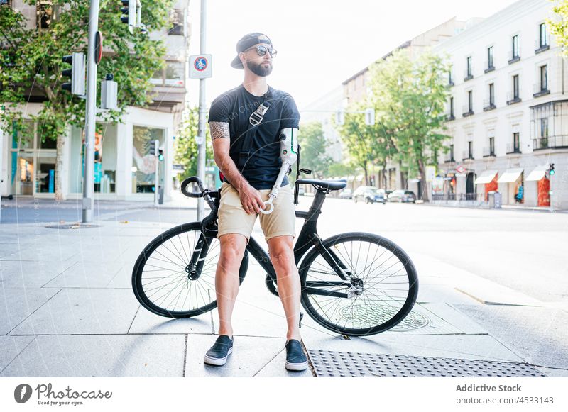 Man with arm prosthesis standing near bike in city man prosthetic artificial limb amputee bionic street male hipster cool handicap bicycle lean sunglasses urban