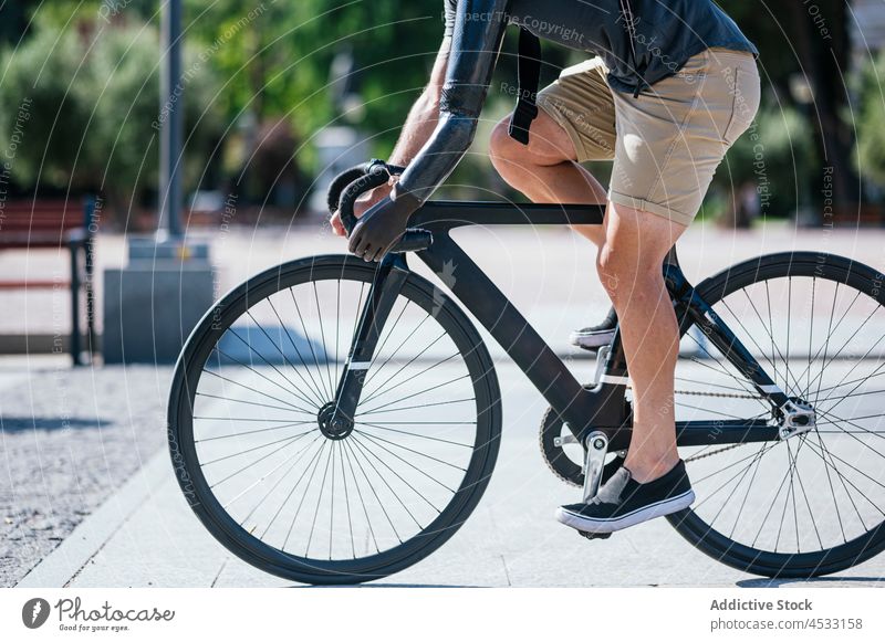 Anonymous man with bionic arm riding bike in city artificial prosthesis handicap prosthetic ride bicycle male street bicyclist summer beard hipster activity
