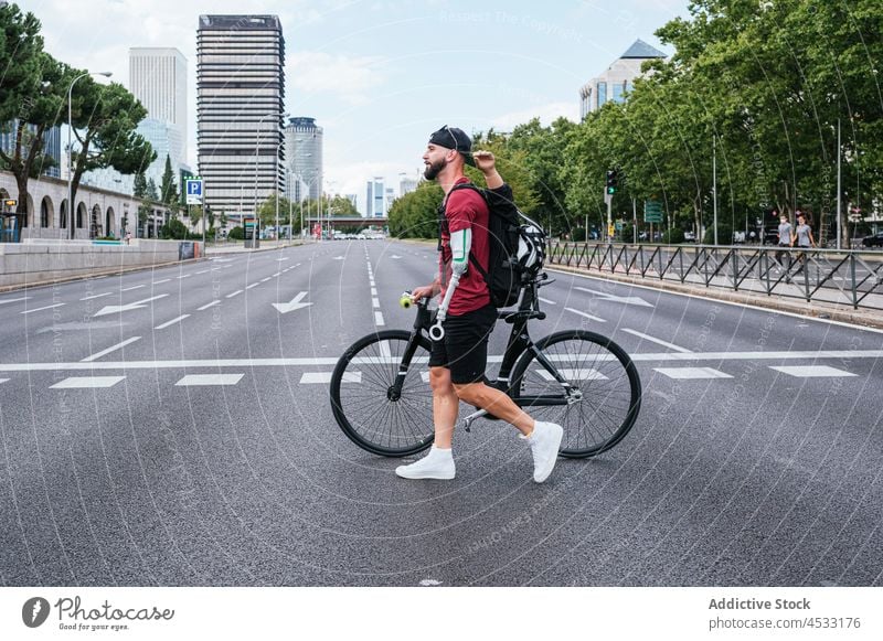 Man with artificial arm walking with bike near road man prosthesis crosswalk amputee limb bionic city male bicycle handicap hipster disable urban bicyclist