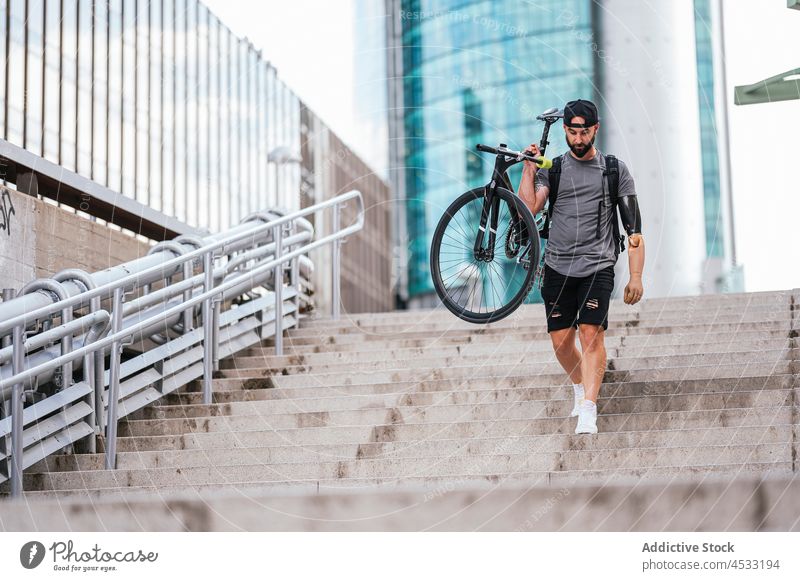 Man with artificial arm walking downstairs with bike man prosthesis bicycle city amputee hipster male handicap disable rubber material step street style cool