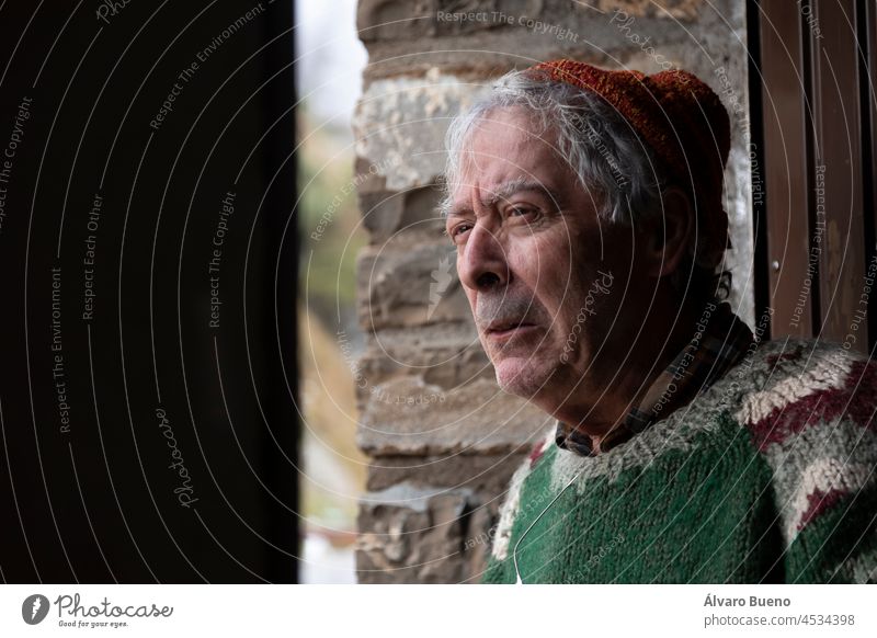 A mountaineer, senior adult man, in his 70s, with handmade woolen sweater, observes the outside from the door of a mountain hut, Pyrenees, Spain shelter