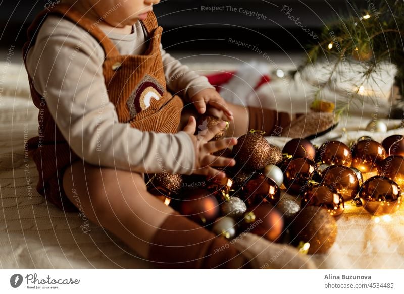 Lifestyle portrait of cute caucasian baby one year old playing with brown baubles on floor at home. Merry Christmas xmas and happy new year 2022 christmas