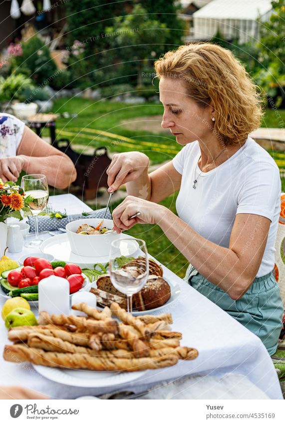 Happy family having a festive dinner or barbecue in the summer garden. Young beautiful woman eating delicious barbecue meat and vegetables. Family dinner in the backyard concept. Lifestyle