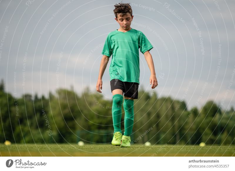 Young football player in sportswear walks thoughtfully on football field Boy (child) Foot ball Football pitch Soccer training soccer field Football boots