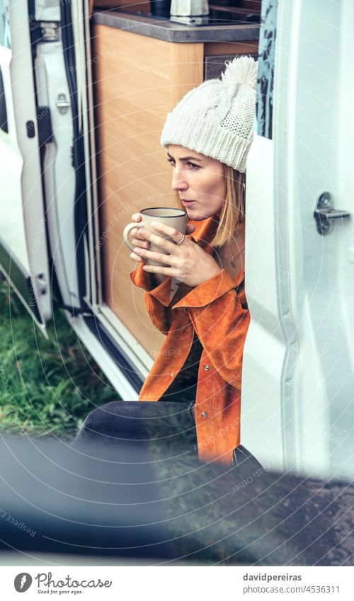 Woman drinking coffee sitting at the door of a campervan woman motorhome winter holding cup blowing hot copy space cold thoughtful morning serious hot coffee