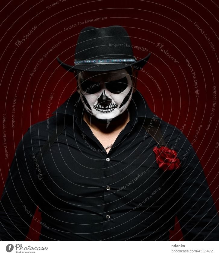 man is painted with a skeleton in a black hat and shirt costume halloween horror death skull holiday face zombie art person celebration dark fear makeup scary