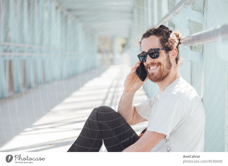 Young hipster man at the airport or bus station waiting while calls someone with the phone, luggage, bags and suitcase. Smiling hipster traveler with sunglasses, copy space, sunny day