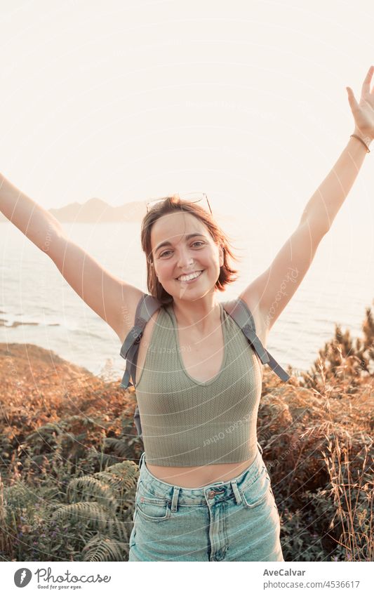 Young backpack girl traveler celebrating reaching his destination hiker during an stunning sunset coastline scenario, hipster traveler concept, beauty landscape. Movement and liberty, nomad life.