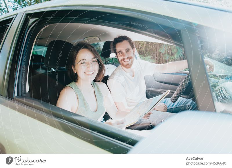 Lovely young couple traveling doing a road trip in car. Road travel, frontal portrait smiling. they are taking a break from driving and looking or checking the map to see the route. Hipster modern couple.