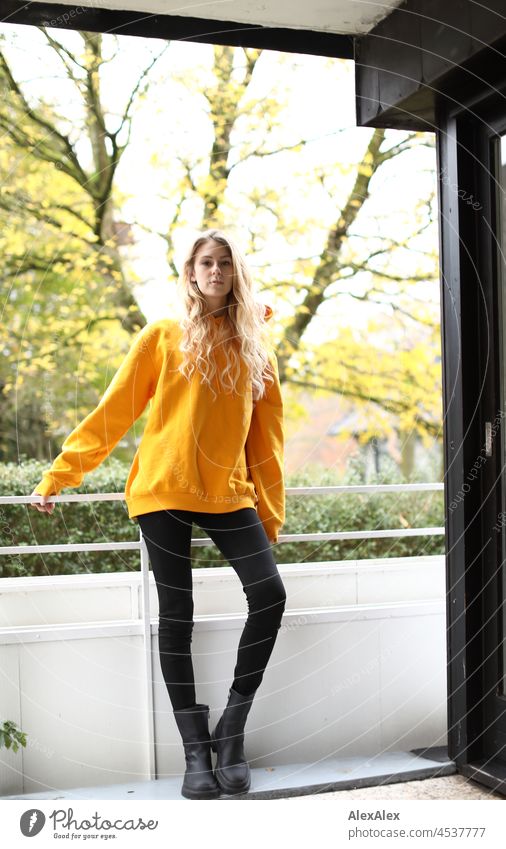 Full body portrait of young slim woman with long blond hair and yellow hoodie on balcony in autumn Woman Young woman Large Blonde Long-haired pretty daintily