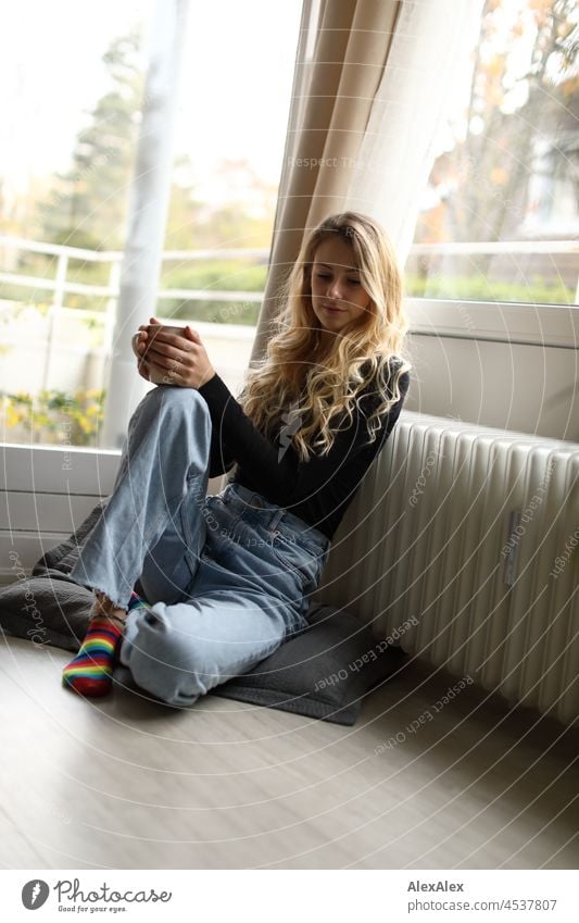 Young slim tall woman with long blonde hair sits in living room in front of balcony window Woman Young woman Large Blonde Long-haired pretty daintily Slim socks