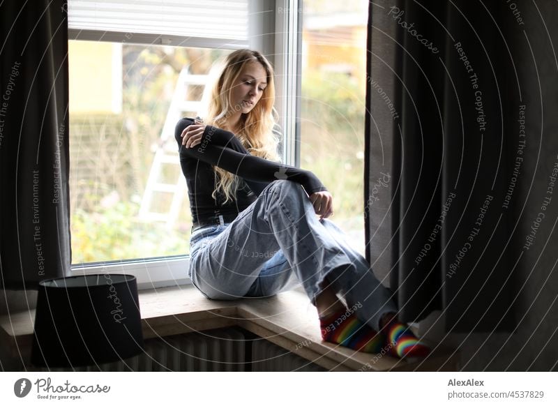 Young slim tall woman with long blonde hair sits in room in front of window Woman Young woman Large Blonde Long-haired pretty daintily Slim socks Striped socks