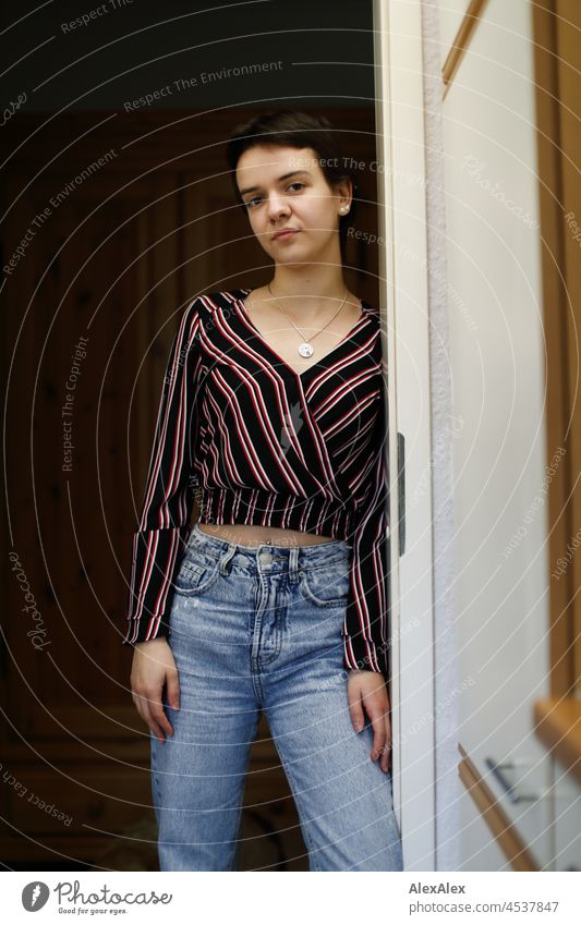 Young woman with short brunette hair leans against the kitchen door Woman short hair Brunette pretty look naturally Authentic Jewellery Chain Slim youthful