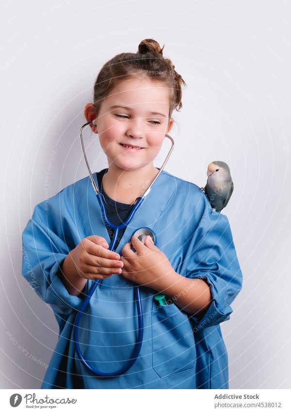Smiling girl in doctor uniform with parrot stethoscope disguise play medical playful childhood instrument bird heartbeat positive studio medicine adorable cute