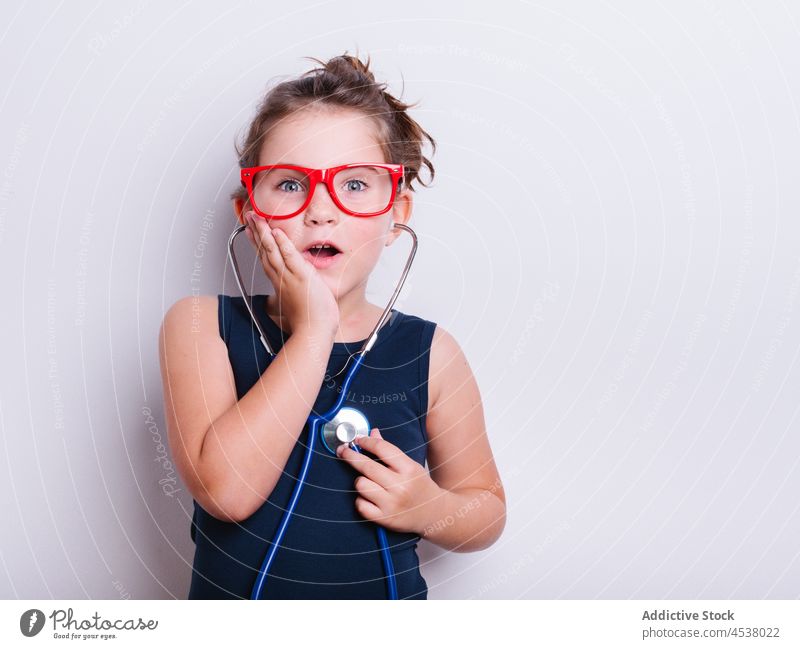 Astonished girl listening to heartbeat doctor stethoscope disguise play medical playful childhood amazed surprise astonish instrument studio eyeglasses medicine