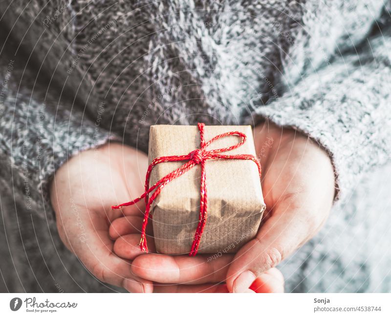 Frau hält ein Geschenk Paket mit roter Schleife in den Händen Weihnachten frau halten Winter pullover grau geburtstag lifestyle teilabschnitt Nahaufnahme Finger