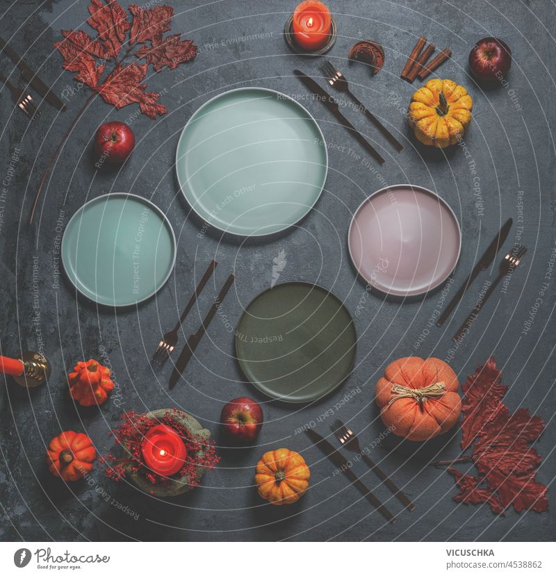 Autumn table settings with various empty plates on dark concrete kitchen background with cutlery, pumpkins, autumn leaves and candles. Preparing seasonal dinner at home with crockery. Top view.