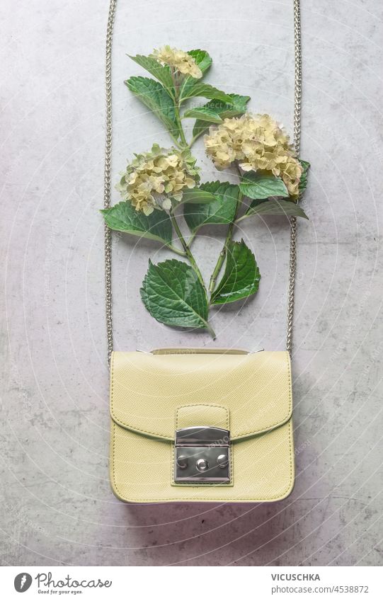 Pale yellow woman hand bag with hydrangea flowers on grey background. Feminine fashion concept with flowers. Top view. pale feminine top view beautiful bloom