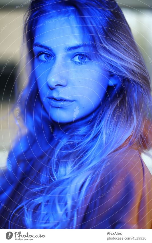 Portrait of a young, slim woman with long blond hair in the living room in front of the window, she is illuminated with blue light Woman Young woman Large