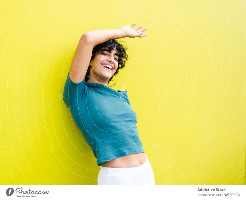 Cheerful woman with hand raised on head near bright wall laugh delight cheerful glad vivid posture individuality expressive glee female positive optimist